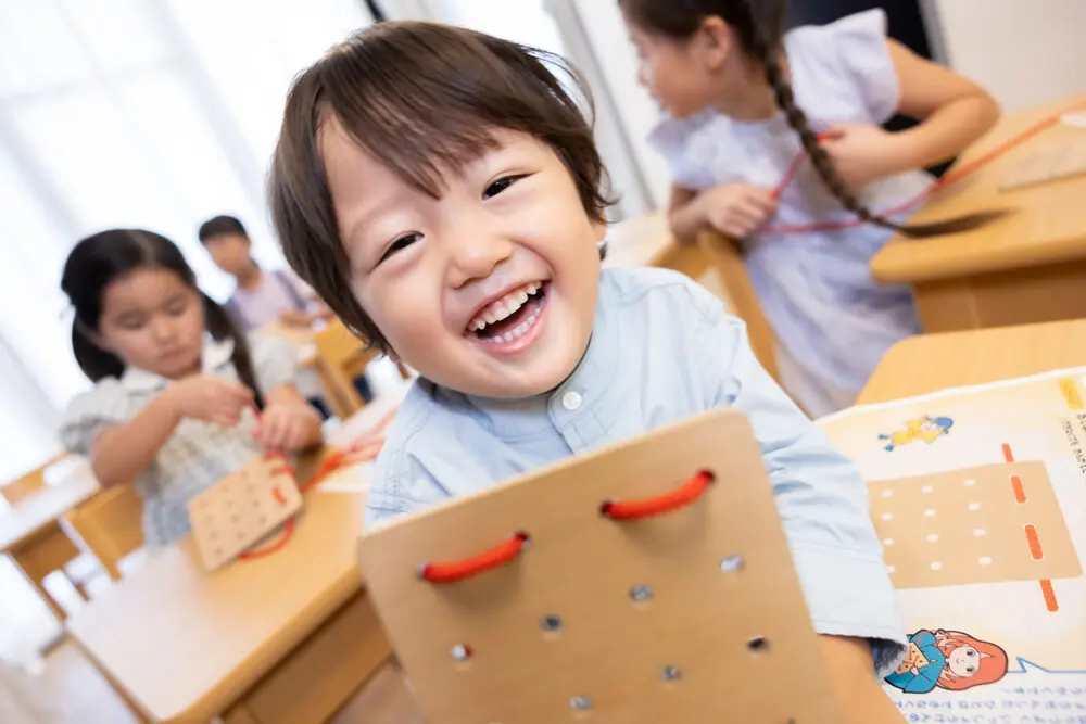 笑顔でひも通しボードの学習に取り組む幼児（楽しみながら思考力と集中力を育む教材シーン）