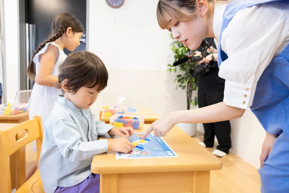 幼児が先生と一緒に教具を使って学ぶ様子(考える力と集中力を育む保育・教育シーン)